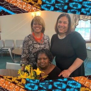 two woman standing behind one woman seated at a table